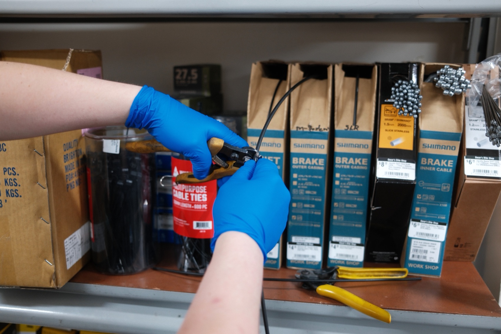Gloved hands installing brake cable housing on a bike in the shop